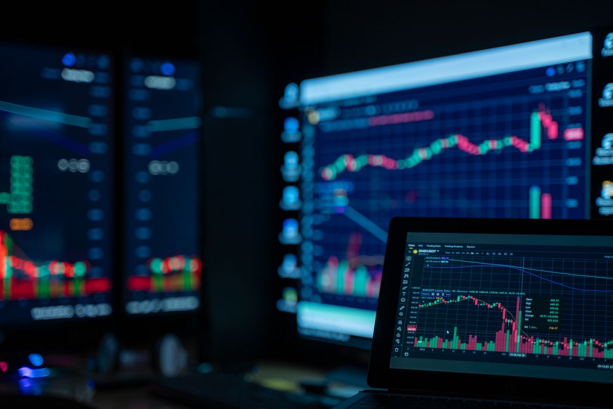 Multiple monitors displaying stock market trading charts in a dimly lit room